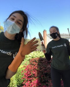 Two college-age girls wearing Lori's Hands t-shirts while volunteer gardening
