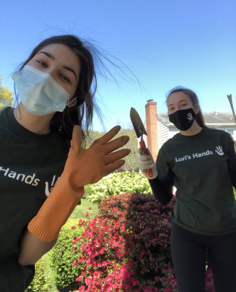 Two college-age girls wearing Lori's Hands t-shirts while volunteer gardening